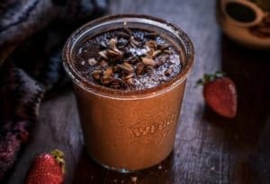 A delicious and decadent drink vegan Rich Dark Chocolate Smoothie made with Botanica Chocolate Perfect Greens. Garnished with toasted coconut flakes, flaked salt, crushed cocoa beans