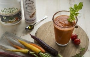 Side shot of vegan and gluten free Vegetable cocktail Smoothie surrounded by Botanica Vanilla Perfect Protein and wholefood carrots