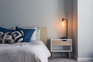 A side picture of bedroom showing half bad and a lit lamp on sidetable