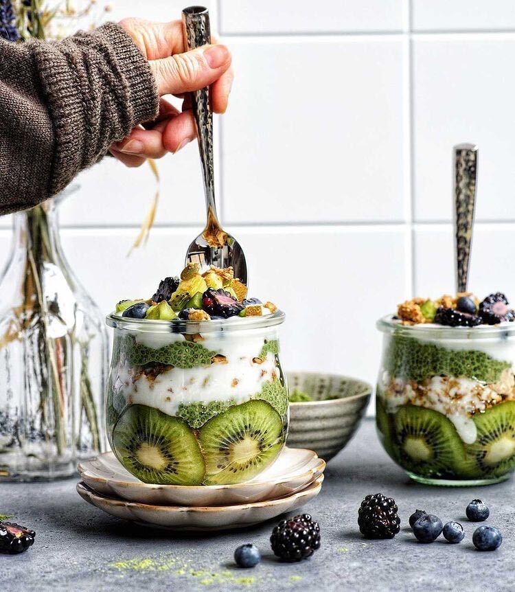 A woman's hand stirring a jar of Kiwi Chia Pudding Parfait made with Botanica's Perfect Greens. 