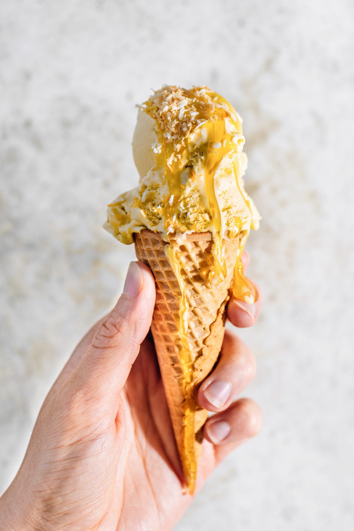 Vegan Lemon Coconut Ice Cream with waffle cone, held in a hand