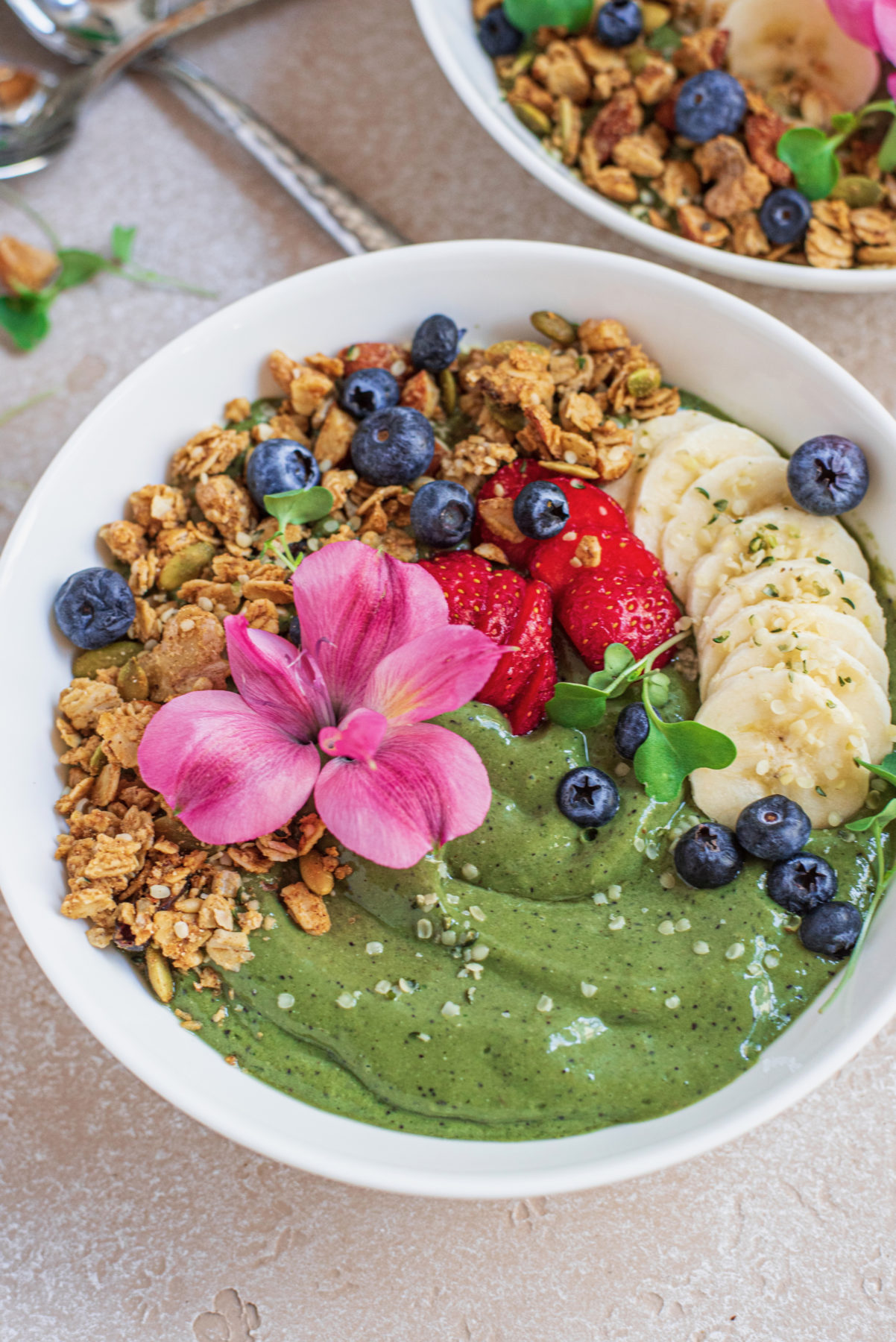 Close up of vegan green smoothie bowl decorated with granola, strawberries, blueberries, banana and quinoa